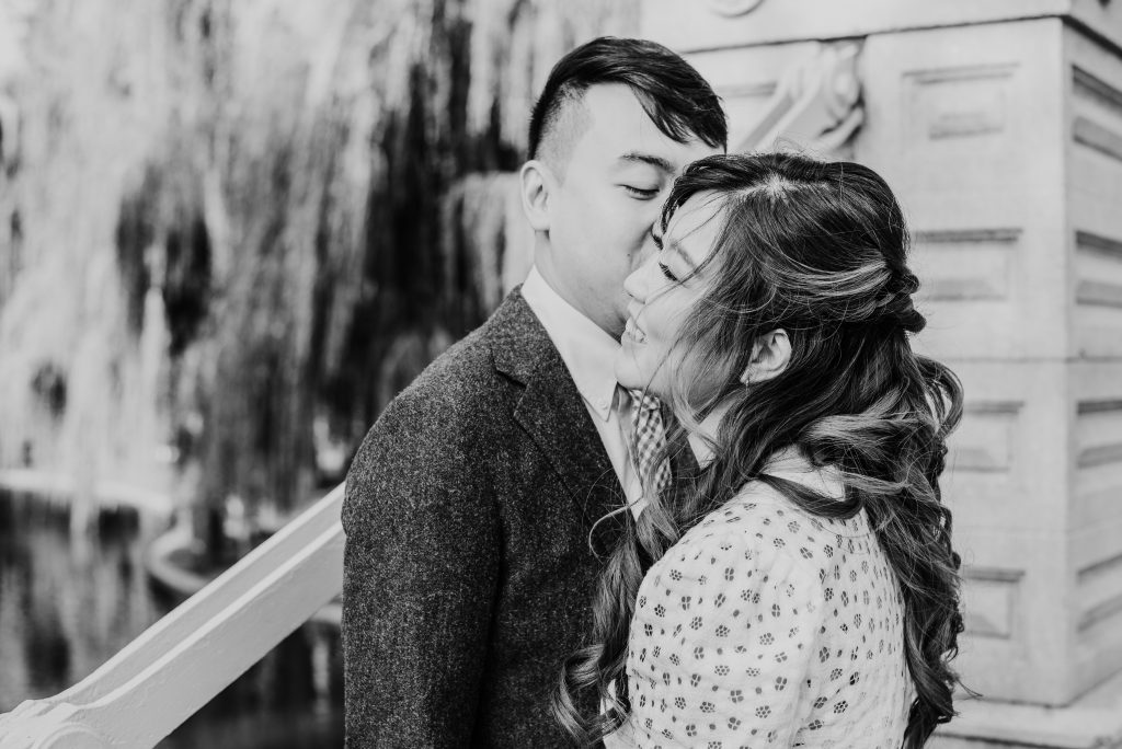 black and white photo of a man kissing his fiancé's cheek on the bridge in the Boston Public Garden during their engagement session 