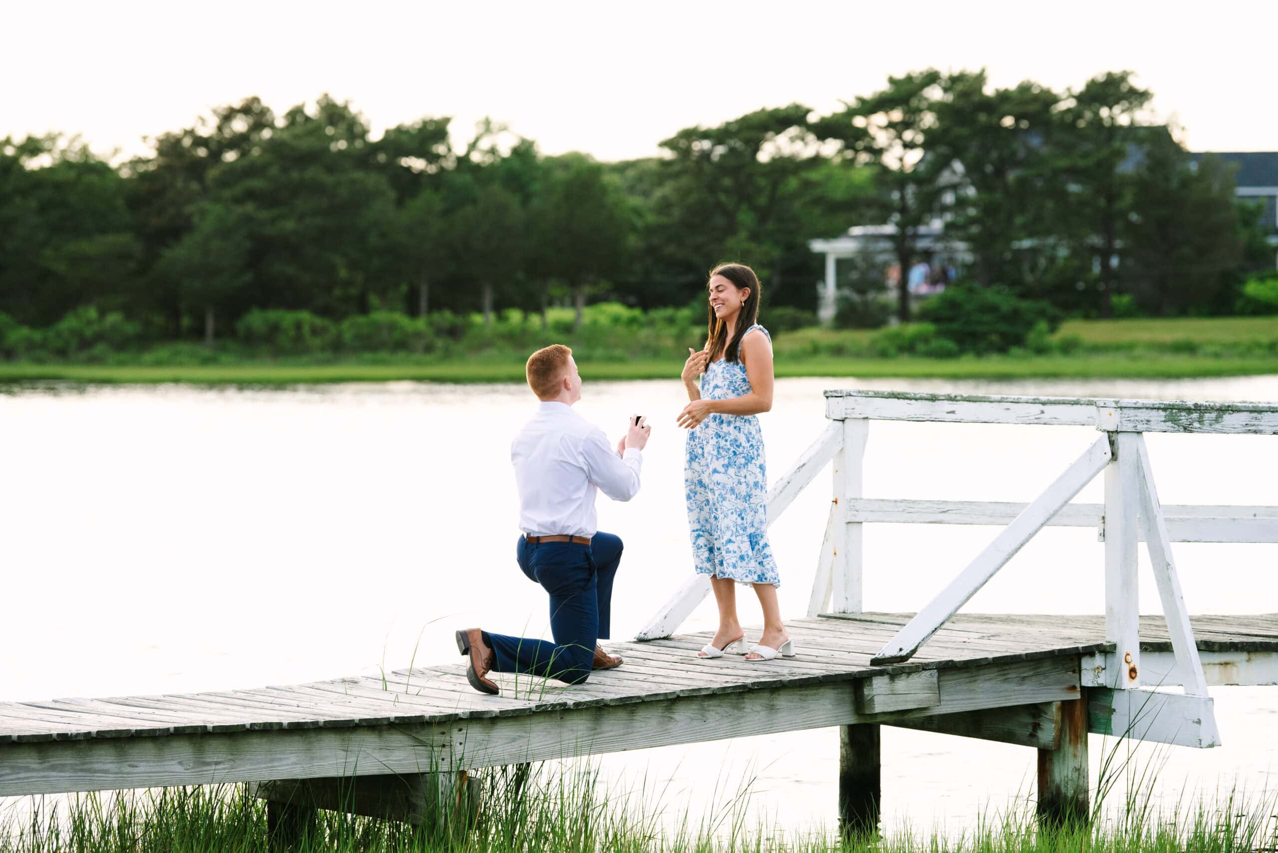 guy on his knee proposing to his girlfriend on a bridge in falmouth massachusetts captured by surprise proposal photographer Meghan Lynch