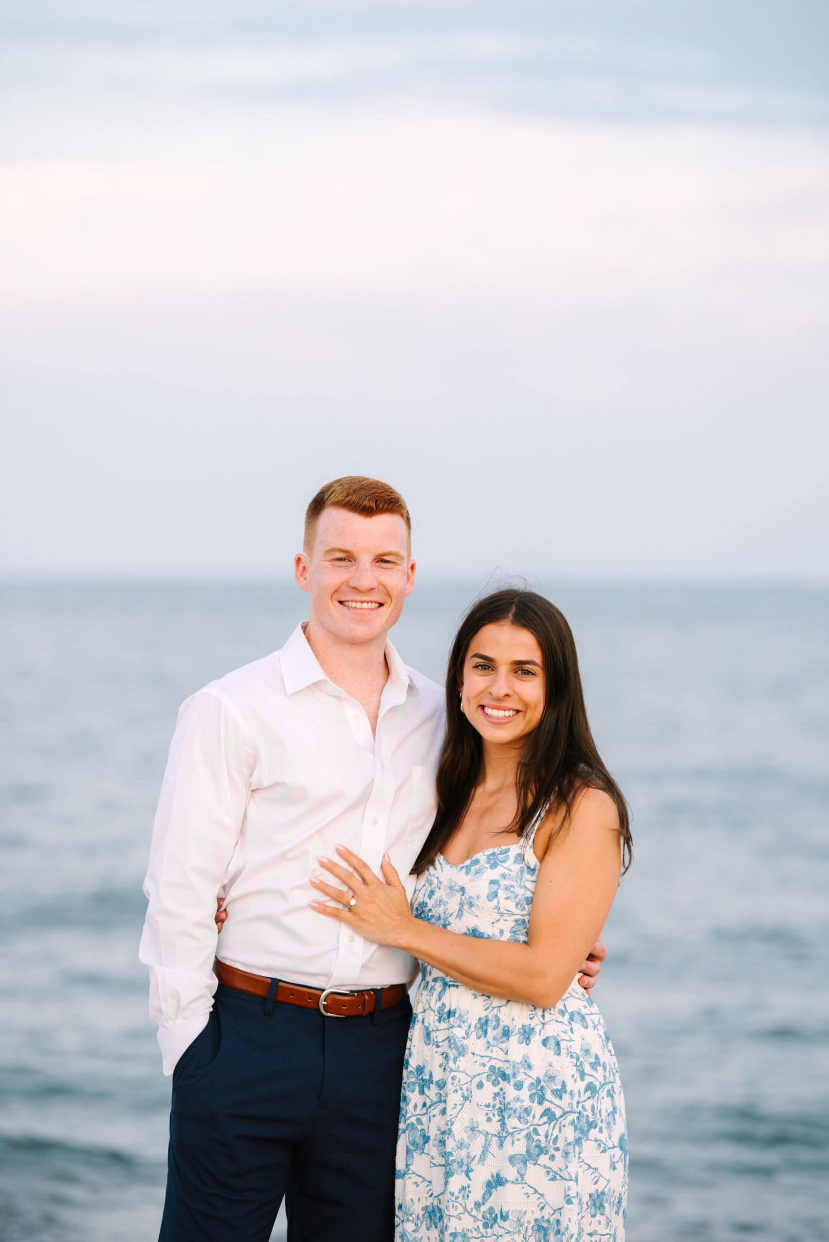 just engaged couple smiling at the camera on menahaunt beach during their falmouth cape cod surprise proposal session