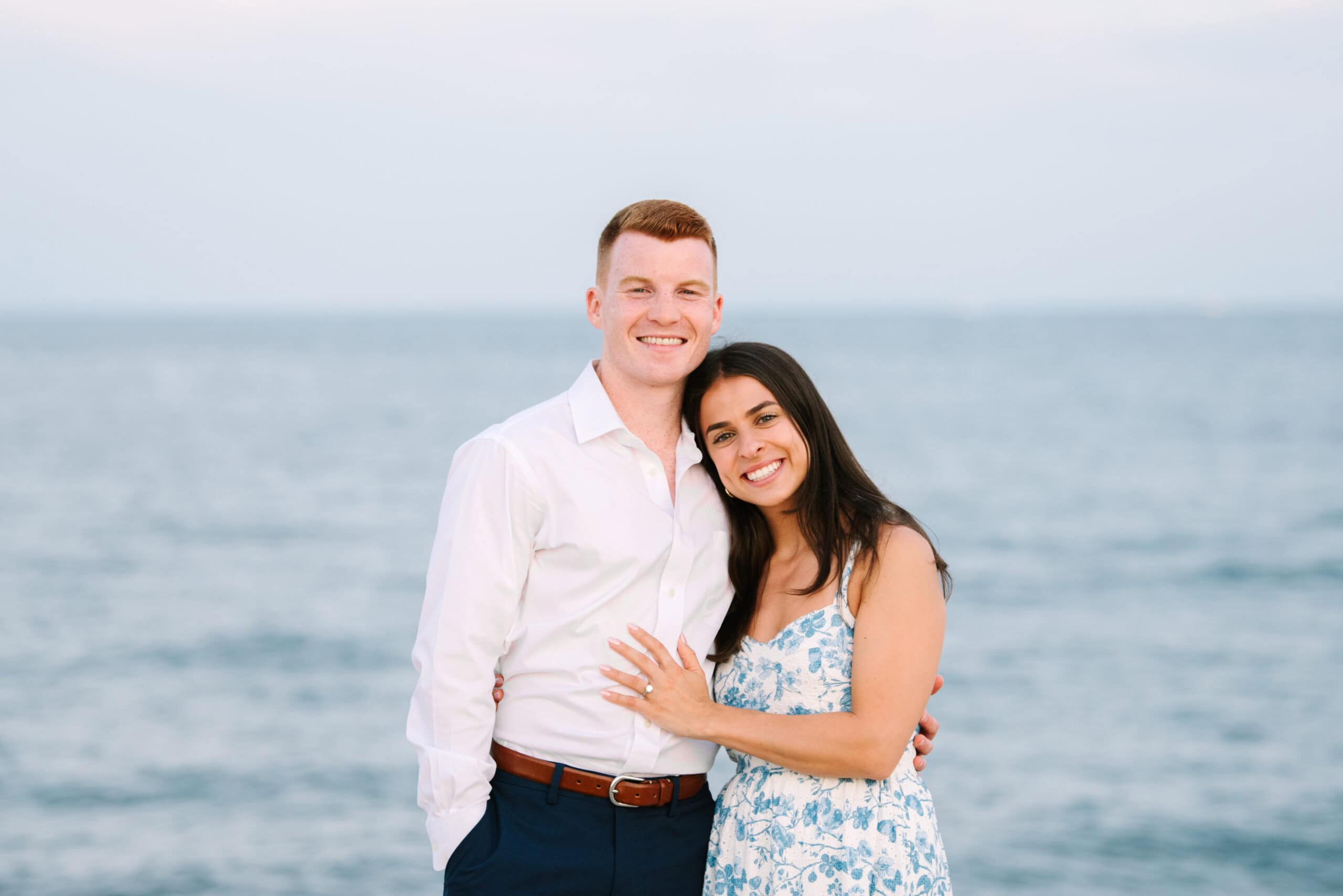 just engaged couple smiling at the camera on menahaunt beach during their falmouth cape cod surprise proposal session