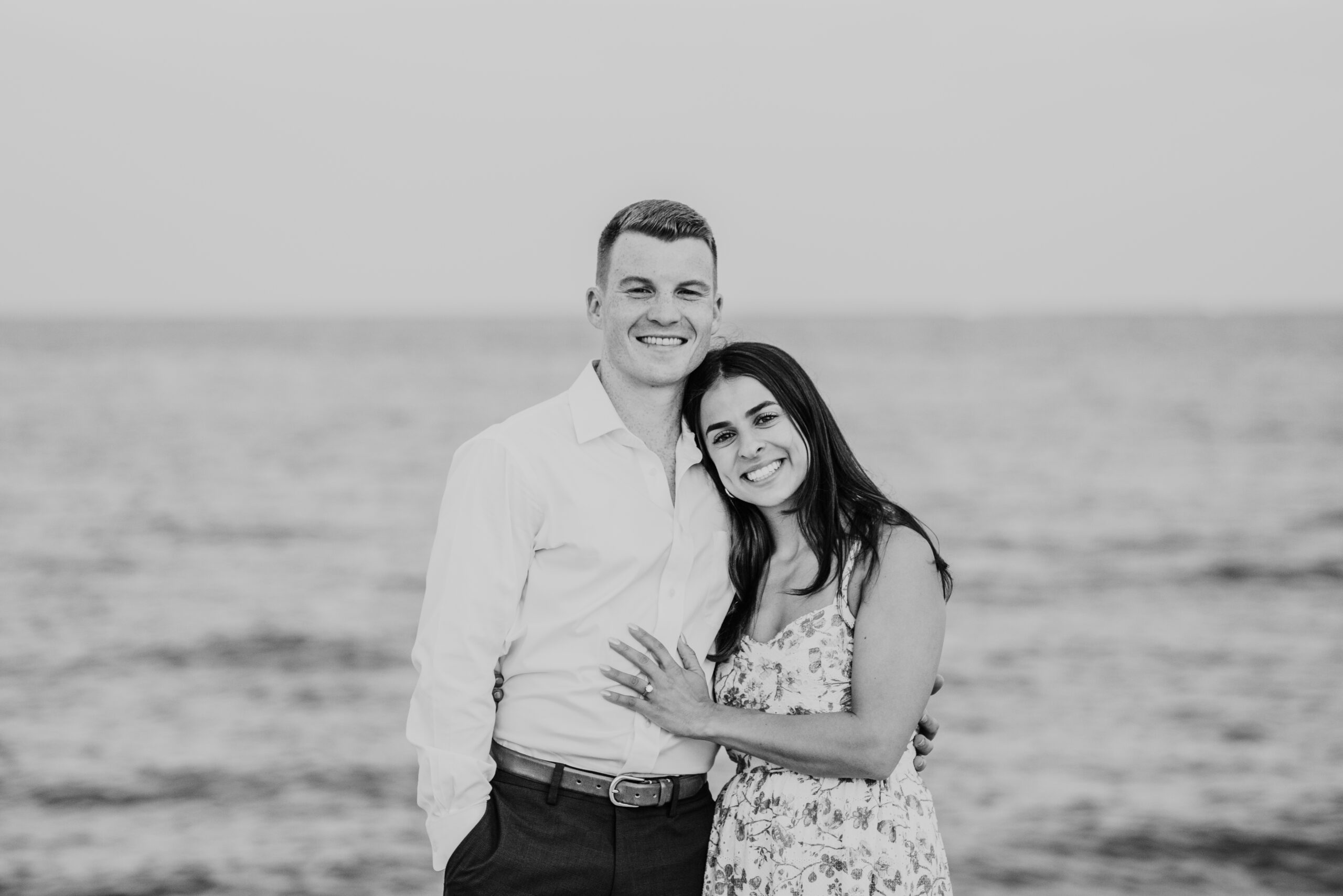 black and white photo of just engaged couple smiling at the camera on menahaunt beach during their falmouth cape cod surprise proposal session