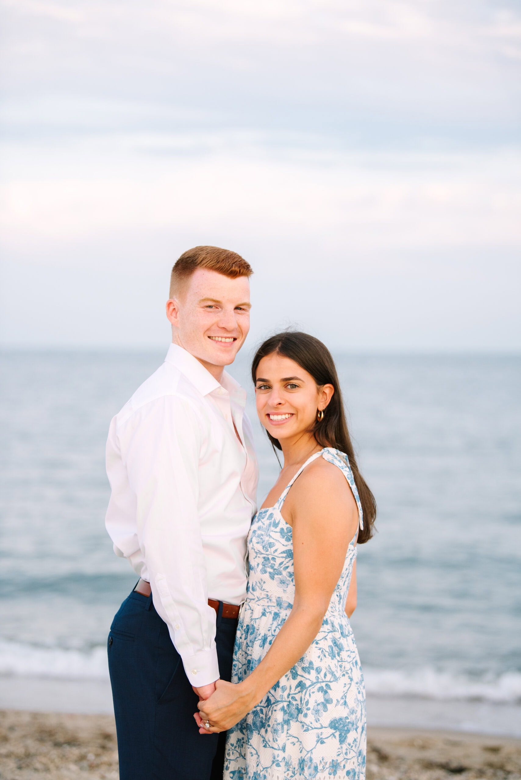 just engaged couple smiling at the camera on menahaunt beach during their falmouth cape cod surprise proposal session