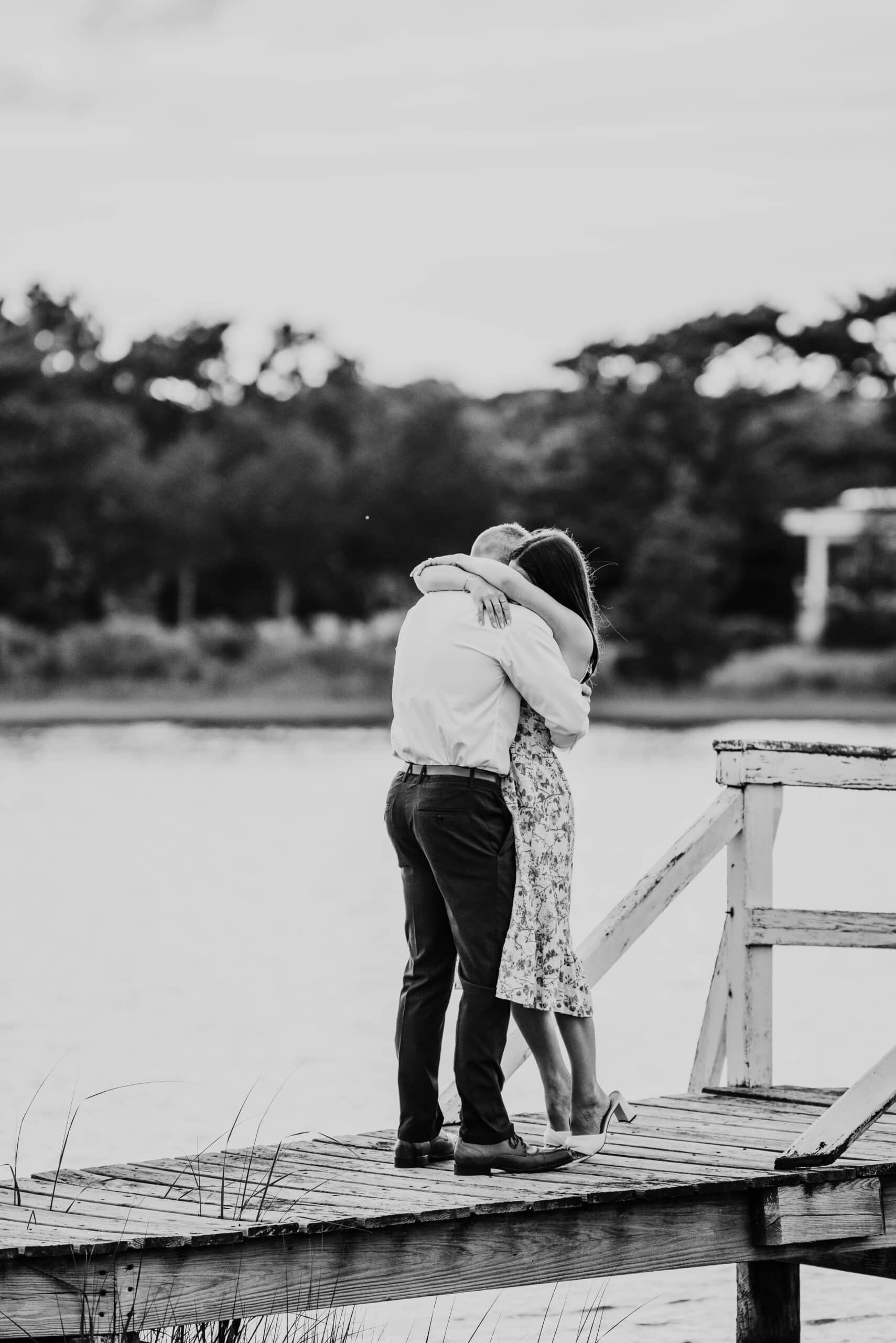 black and white photo of just engaged couple hugging on a white bridge during a falmouth proposal in massachusetts