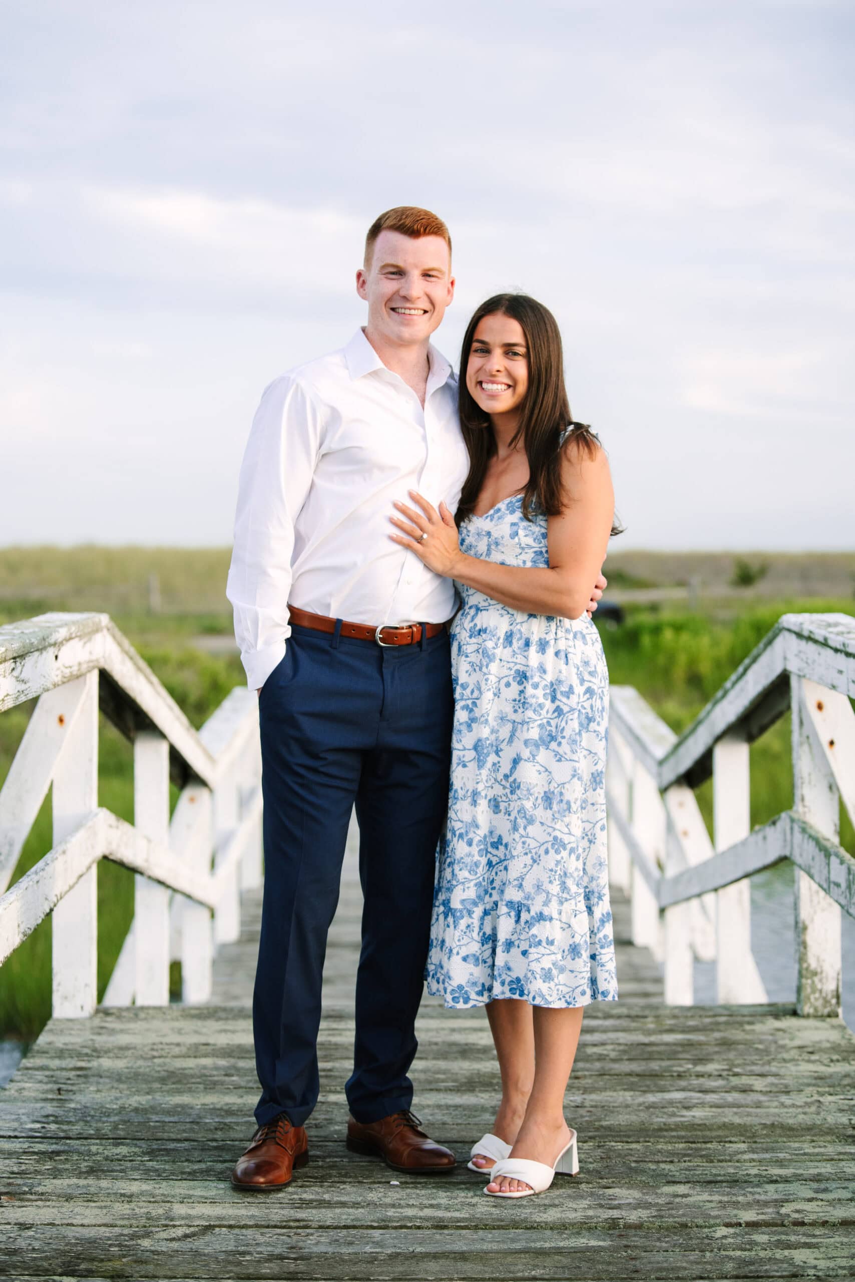 newly engaged couple smiling at the camera on a bridge after a cape cod surprise proposal