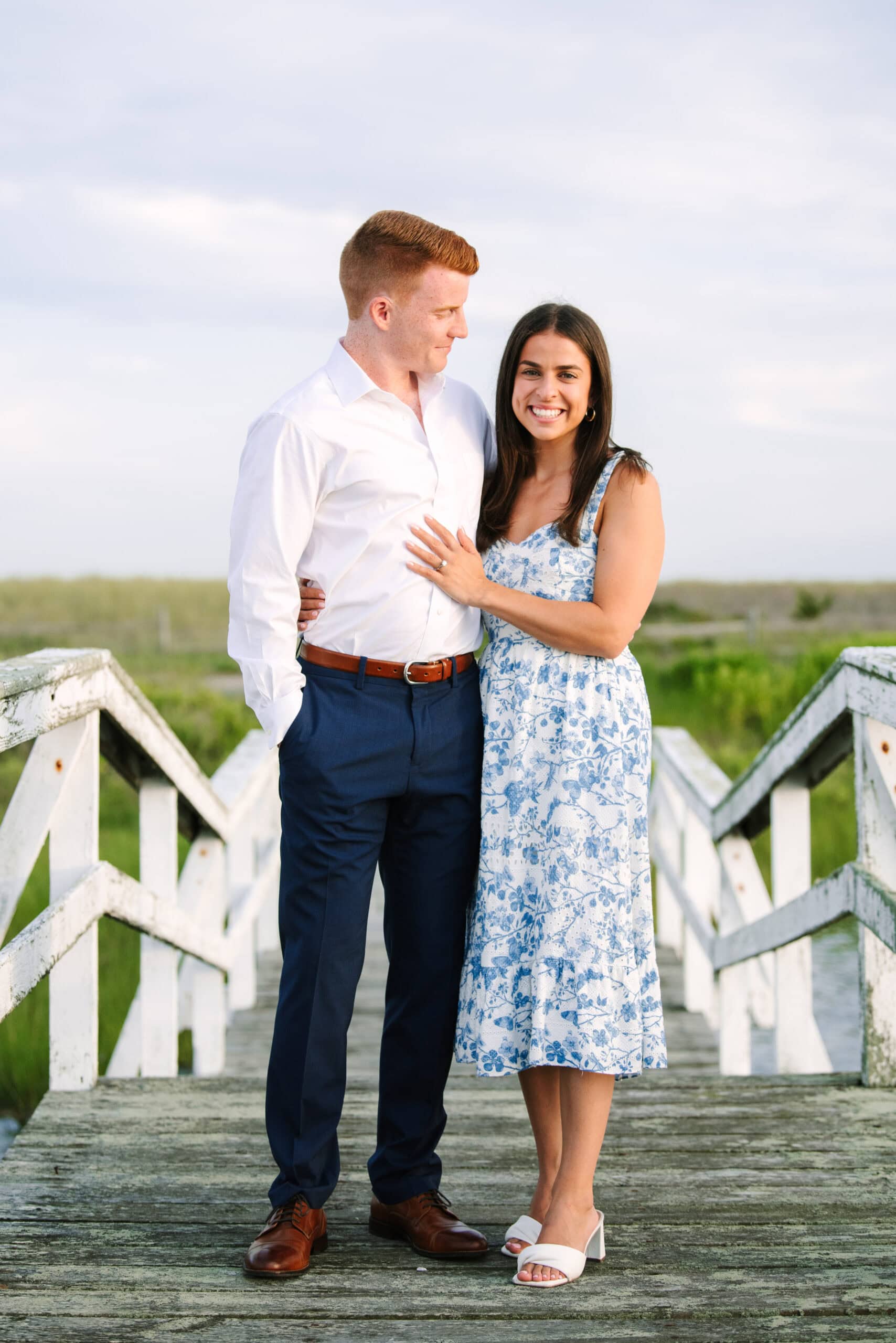 newly engaged couple smiling at the camera on a bridge after a cape cod surprise proposal