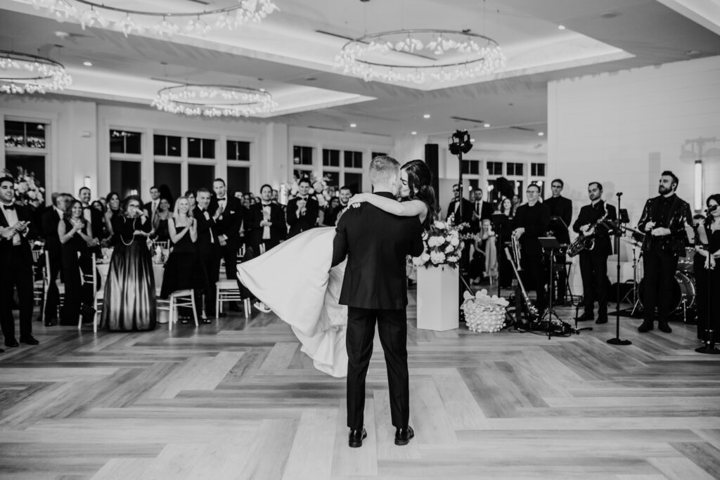 black and white photo of the groom lifting and kissing the bride during their first dance at their wychmere beach club wedding reception on Cape Cod 