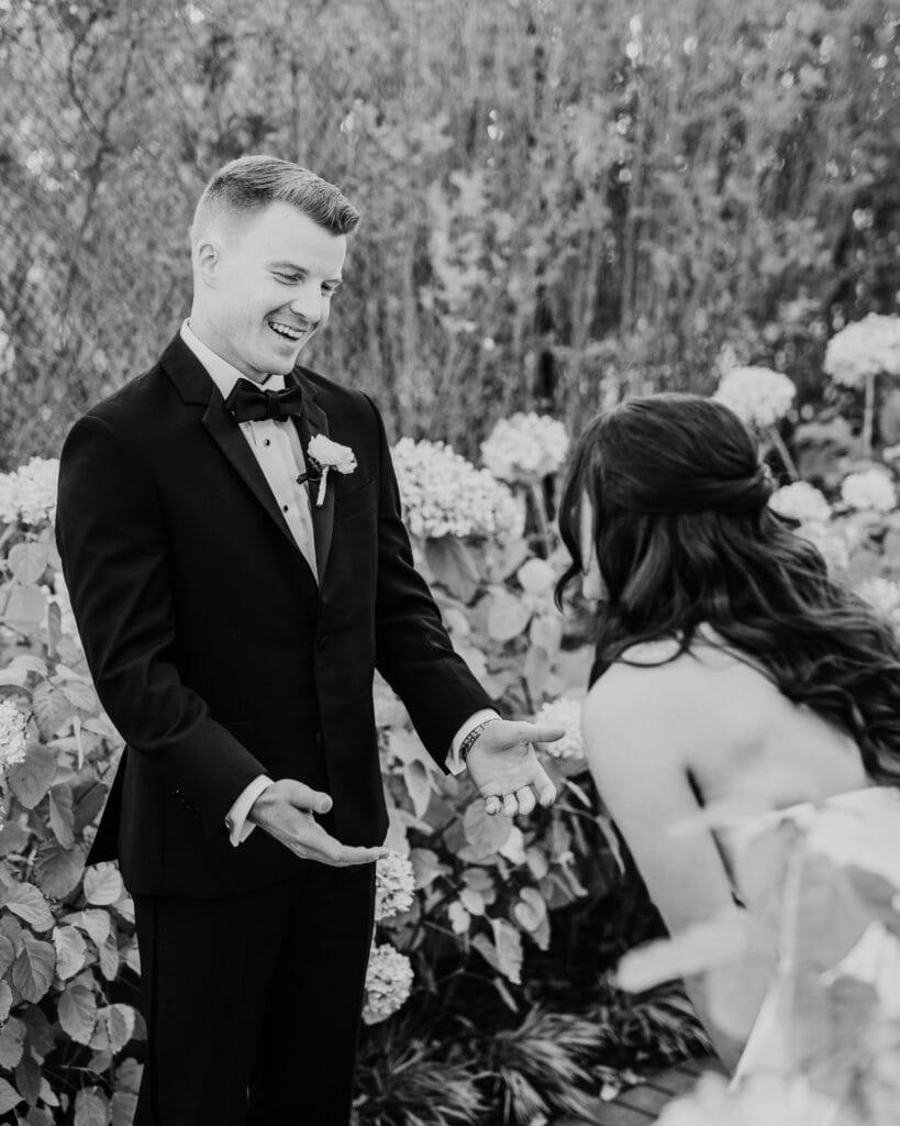 black and white photo of groom reacting to the first look by hydrangeas during their wychmere beach club dune wedding ceremony on Cape Cod