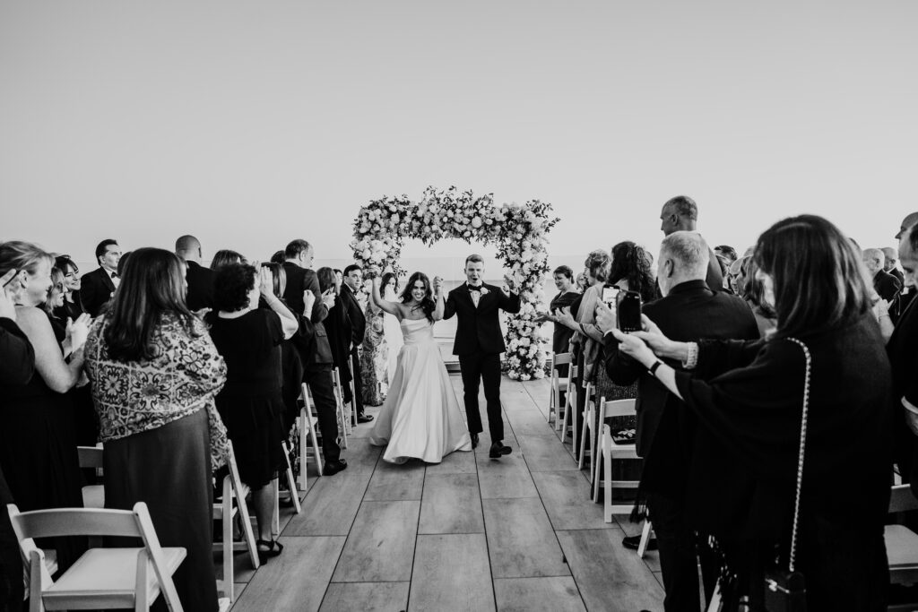 black and white photo of the bride and groom walking back down the aisle after their wychmere beach club wedding ceremony on the dune rooftop during their cape co wedding