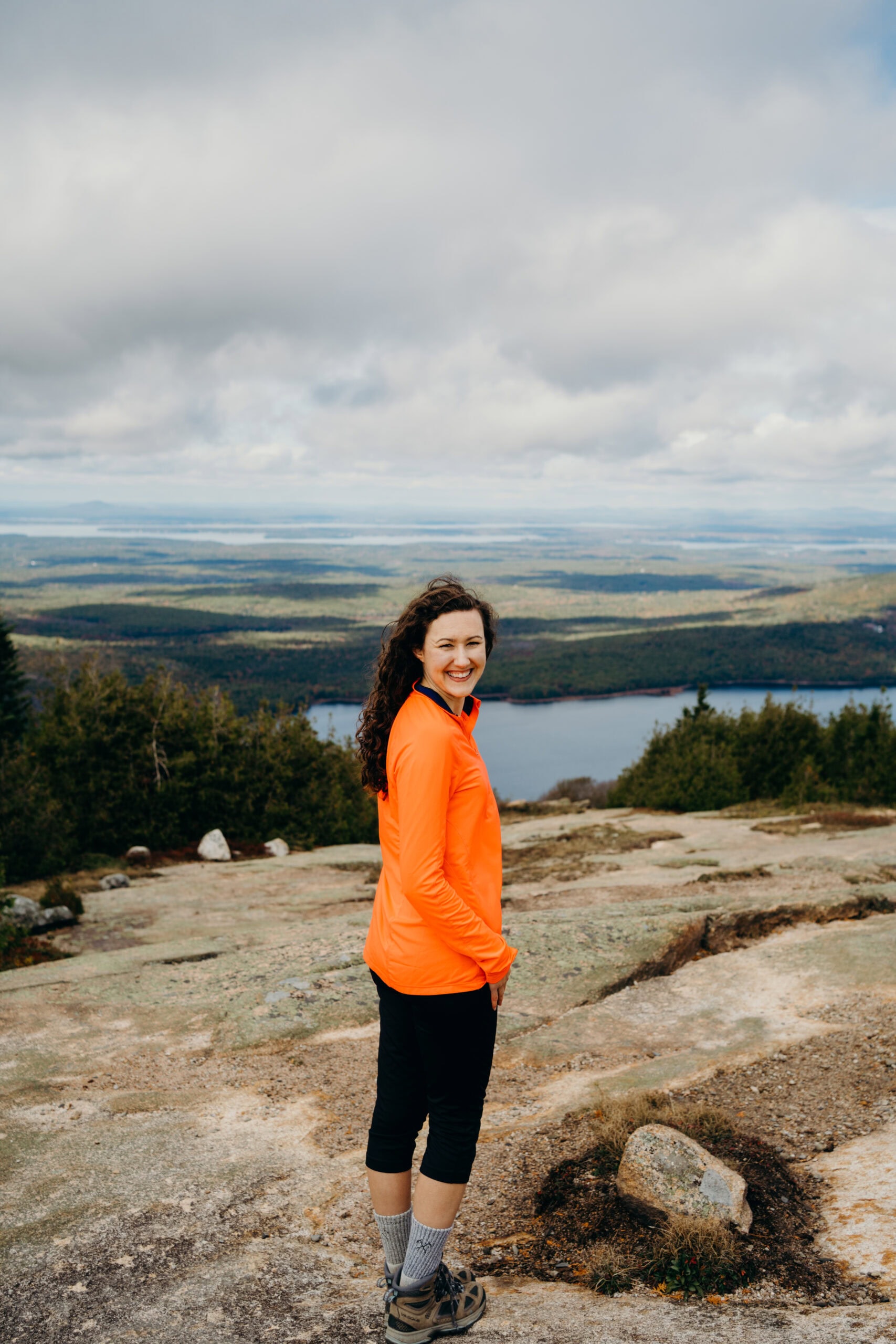 acadia national park elopement photographer Meghan Lynch smiling at the camera on top of Cadillac Mountain in Maine