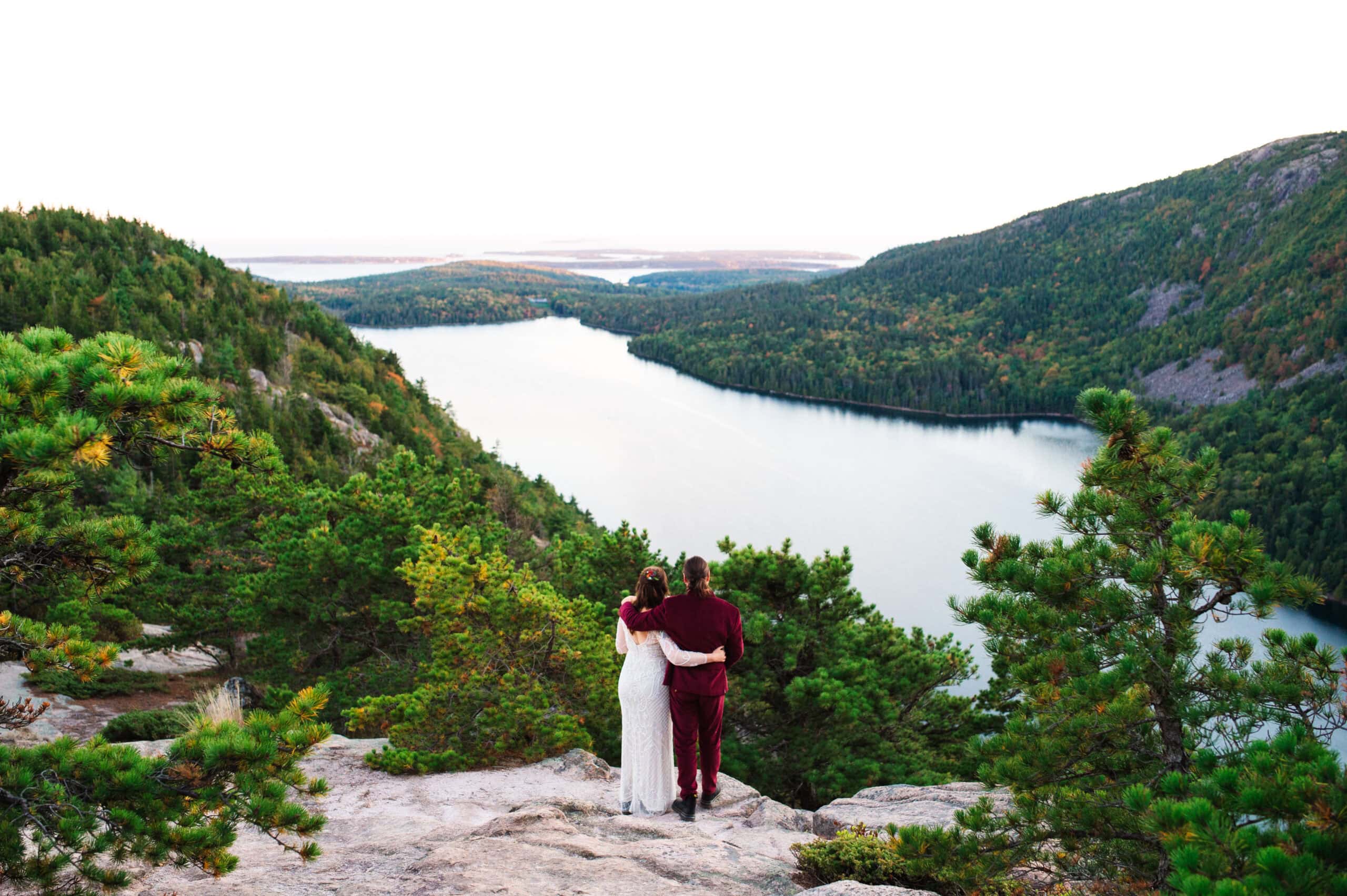 bride and groom with backs to the camera looking at the view from their sunset Acadia national park elopement on a mountain in Maine