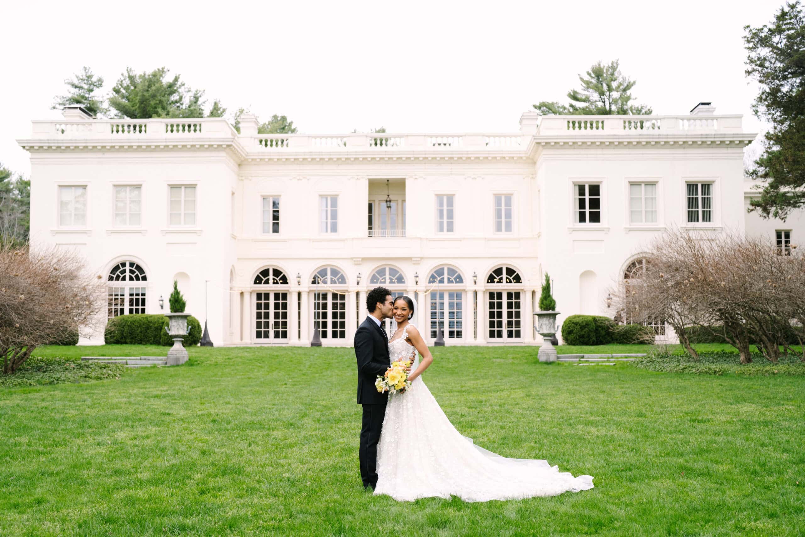 wide shot of the wadsworth mansion with the groom kissing the bride on the cheek