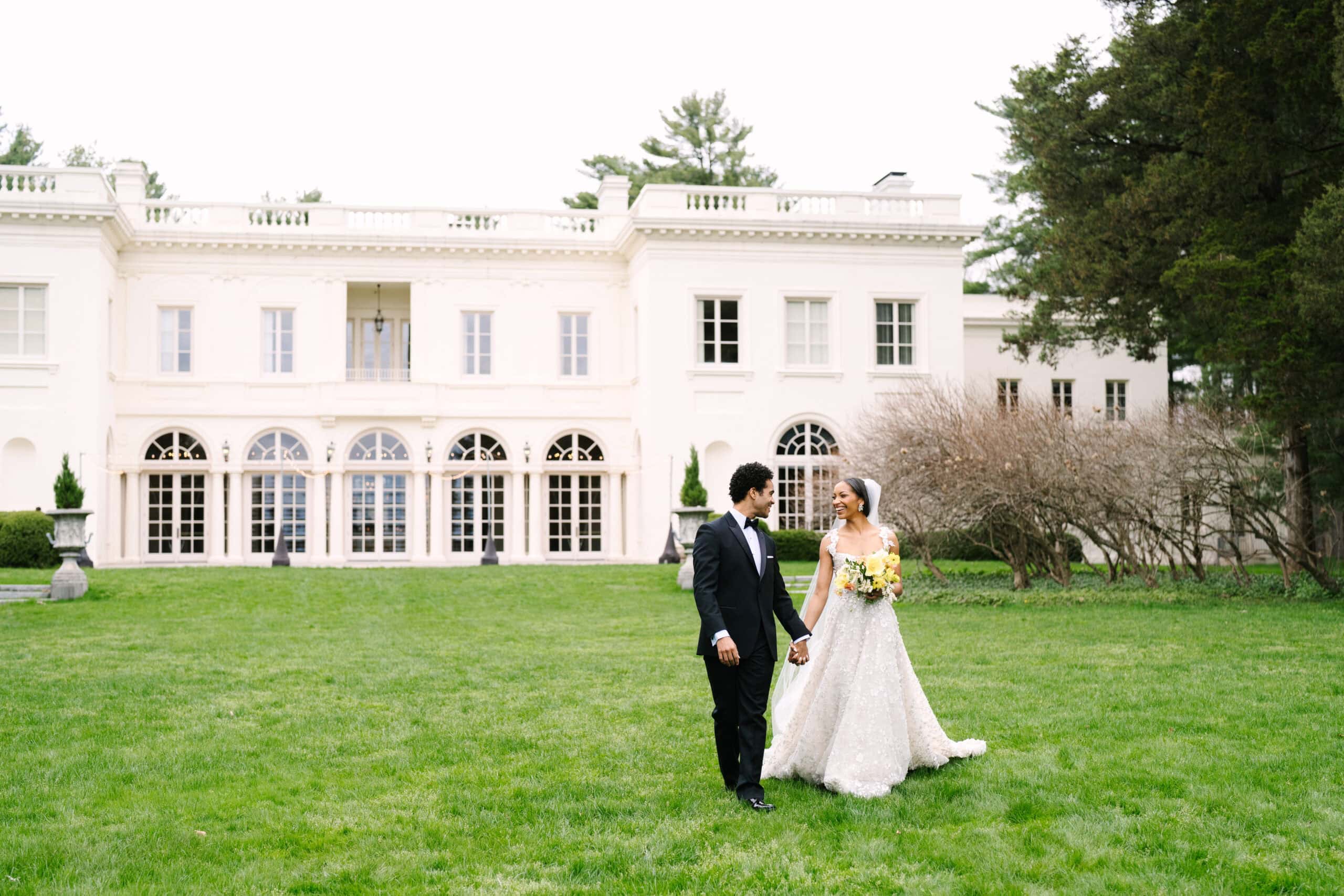 bride and groom holding hands walking with the wadsworth mansion behind them