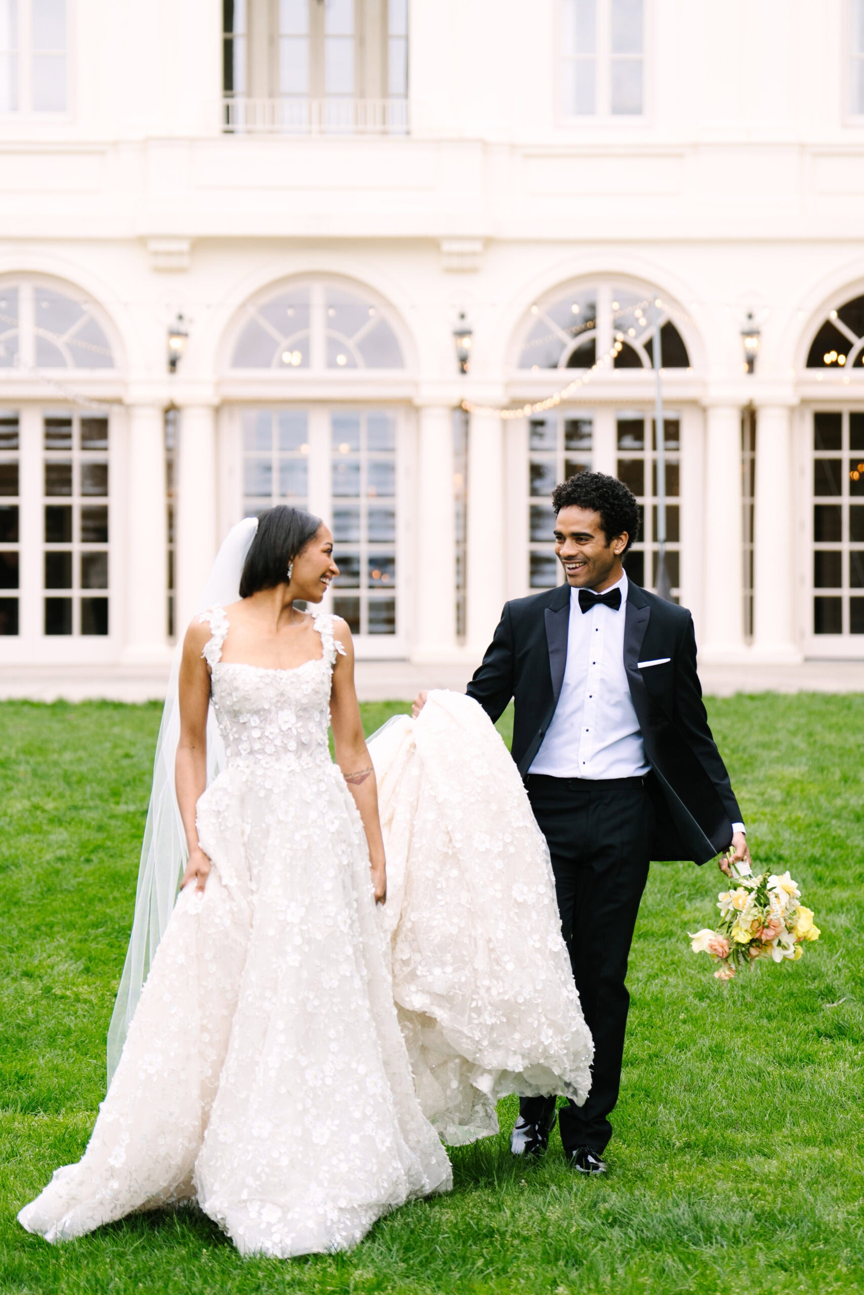 bride and groom walking while he is holding the end of her dress and bouquet during a wadsworth mansion wedding