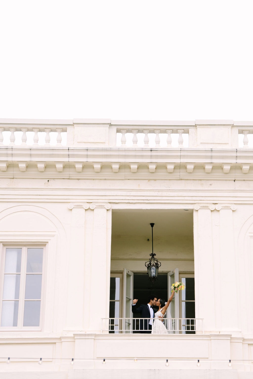 bride and groom kissing with raised hands on the second floor balcony of the wadsworth mansion during their connecticut wedding