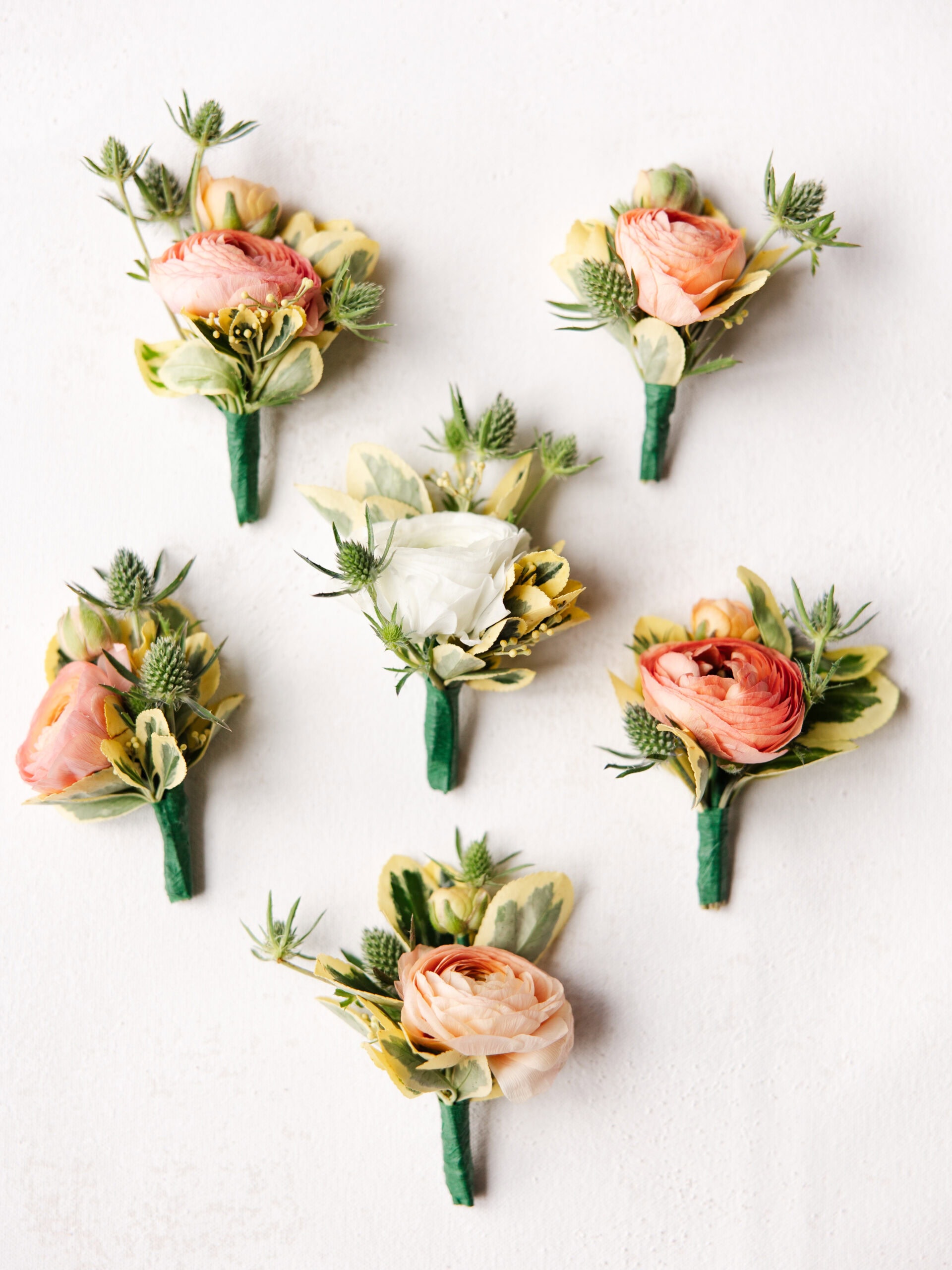 six boutonnieres on a chasing stone styling mat for a wedding flat lay