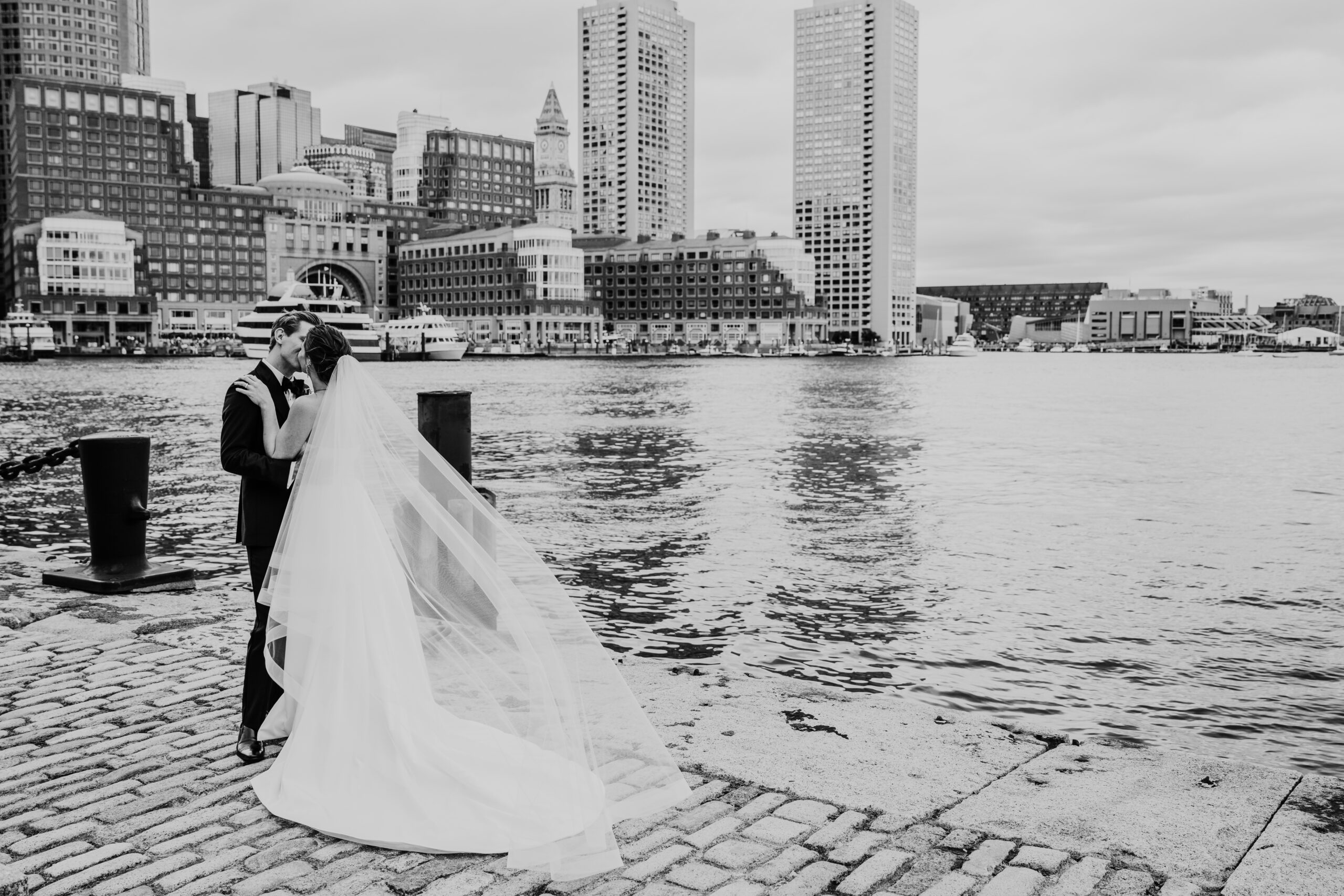 black and white photo of the bride and groom kissing with the boston skyline behind them during their ica boston wedding