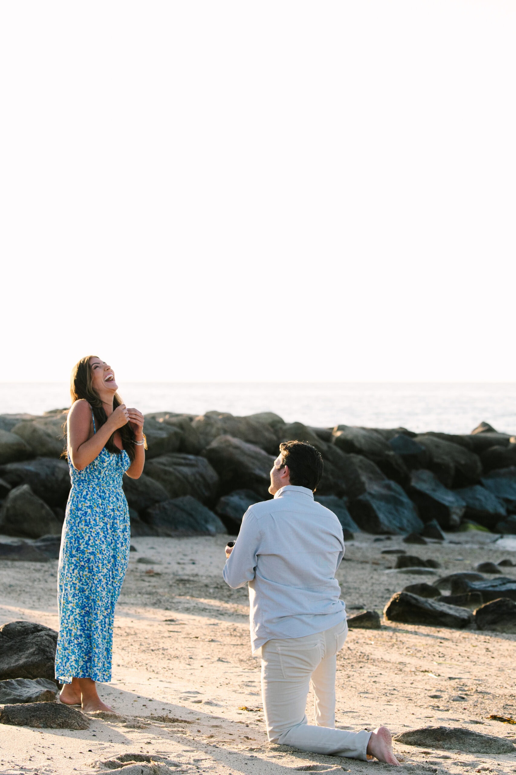 girlfriend smiling as her boyfriend proposes to her on point of rocks landing beach on cape cod