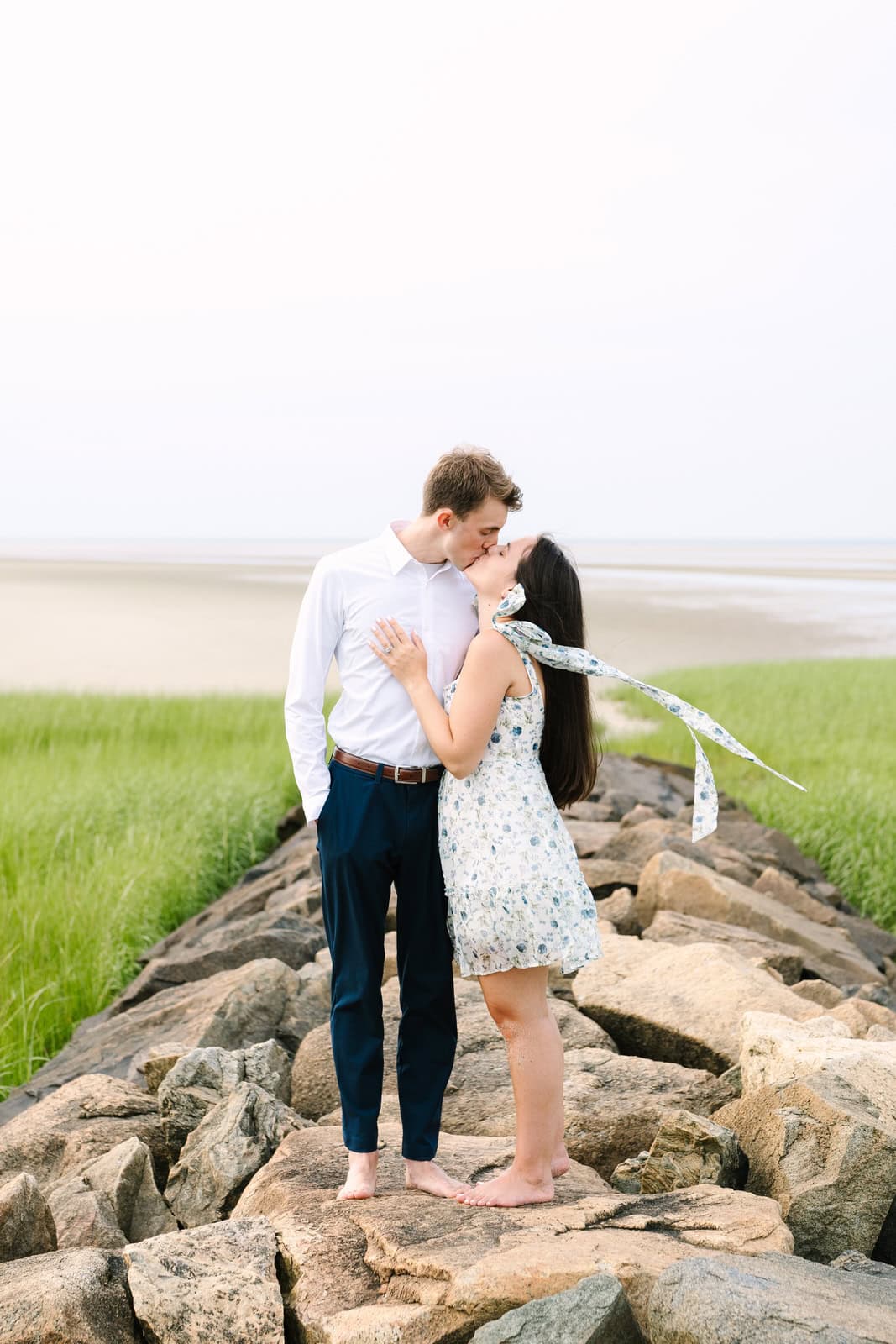 couple kissing on a rock jetty at paines creek beach in brewster for their cape cod engagement portraits