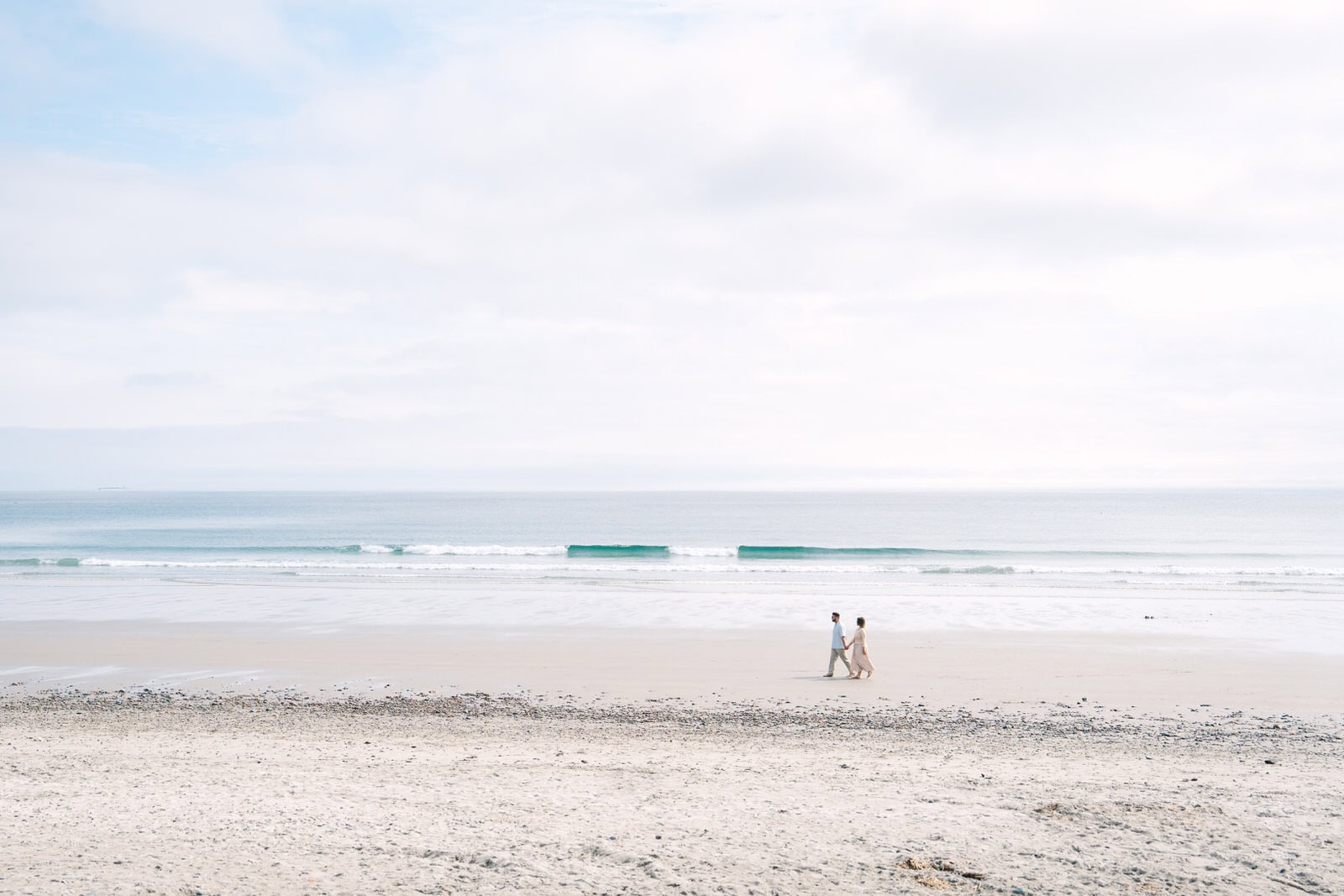 wide landscape portrait of newly engaged couples walking the beach with the ocean behind them during their Nantasket Beach engagement session