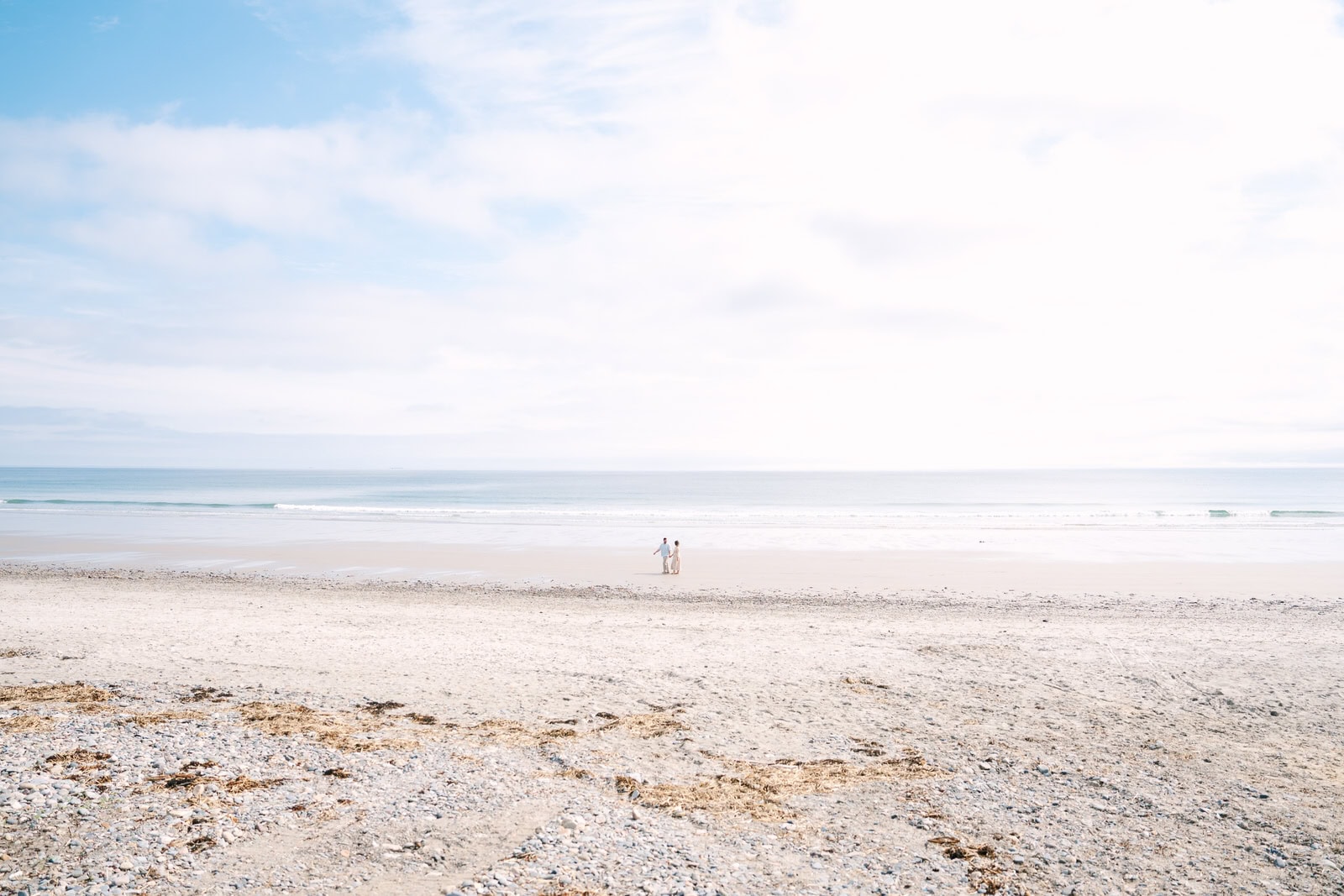 far away landscape shop of an engaged couple walking nantasket beach with the ocean behind them