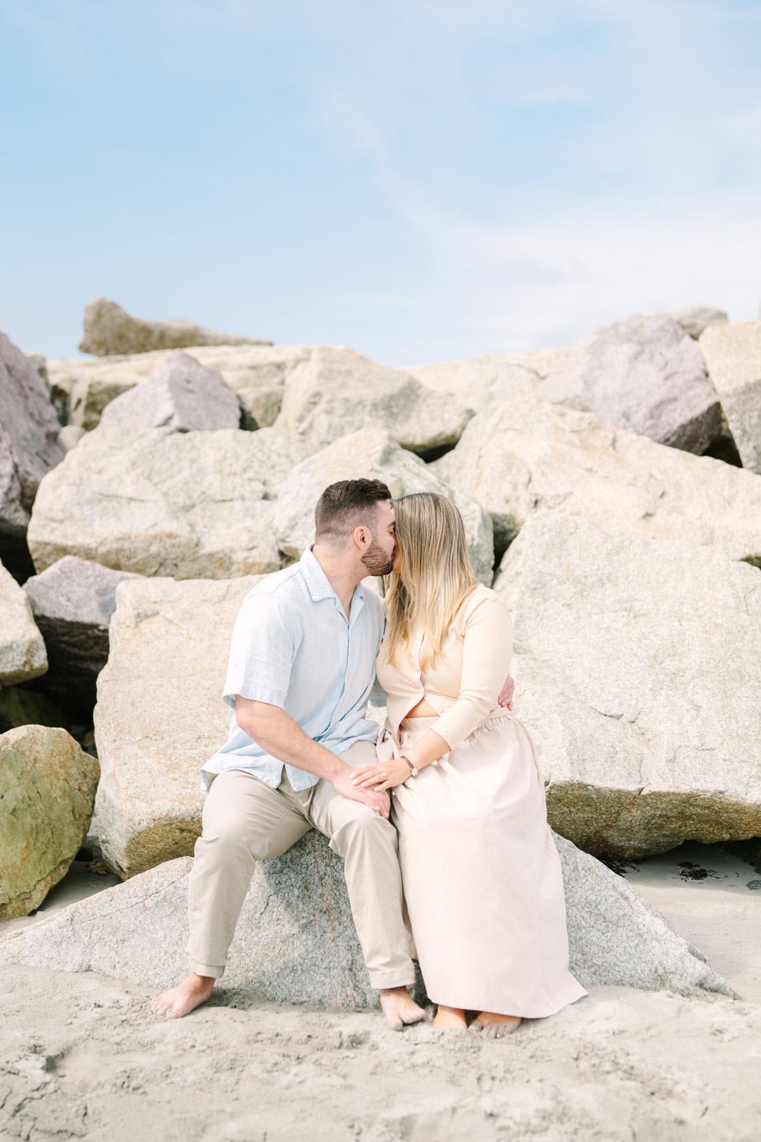 engaged couple sitting on rocks kissing during their nantasket beach engagement session